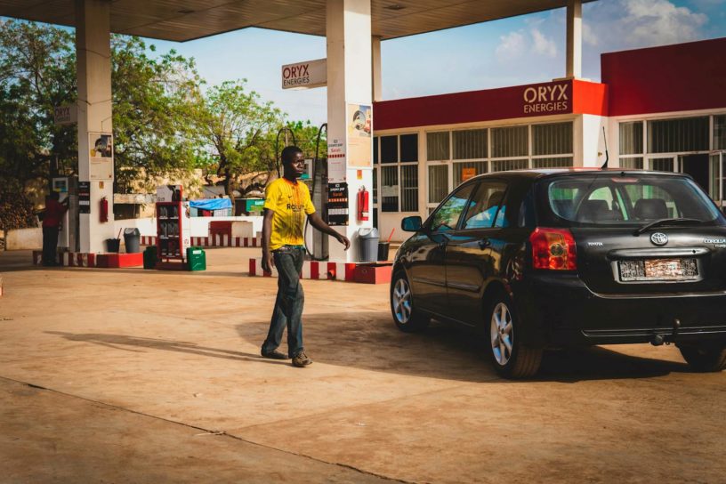 Man at a gas station fueling a black car under the bright daylight.